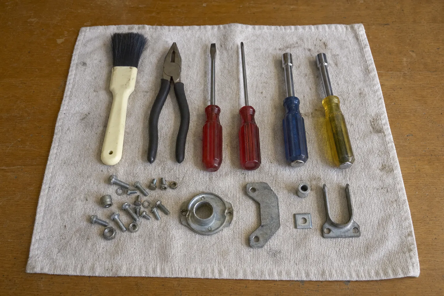 Paintbrush, pliers, two screwdrivers and two nut drivers laid out above a flanged housing, a curved bracket and a U-shaped clip